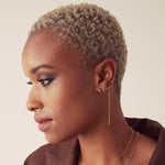 Woman with short, styled hair wearing earrings and a necklace against a neutral background