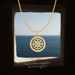 Gold compass necklace with a diamond on a stone ledge with ocean view