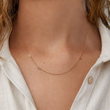 Necklace with small gold beads worn by a person with a white shirt.