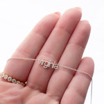 Silver necklace with 'virginia' pendant on a hand against a white background