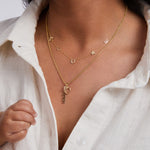 Close-up of a person wearing a gold necklace with various charms against a white shirt background.