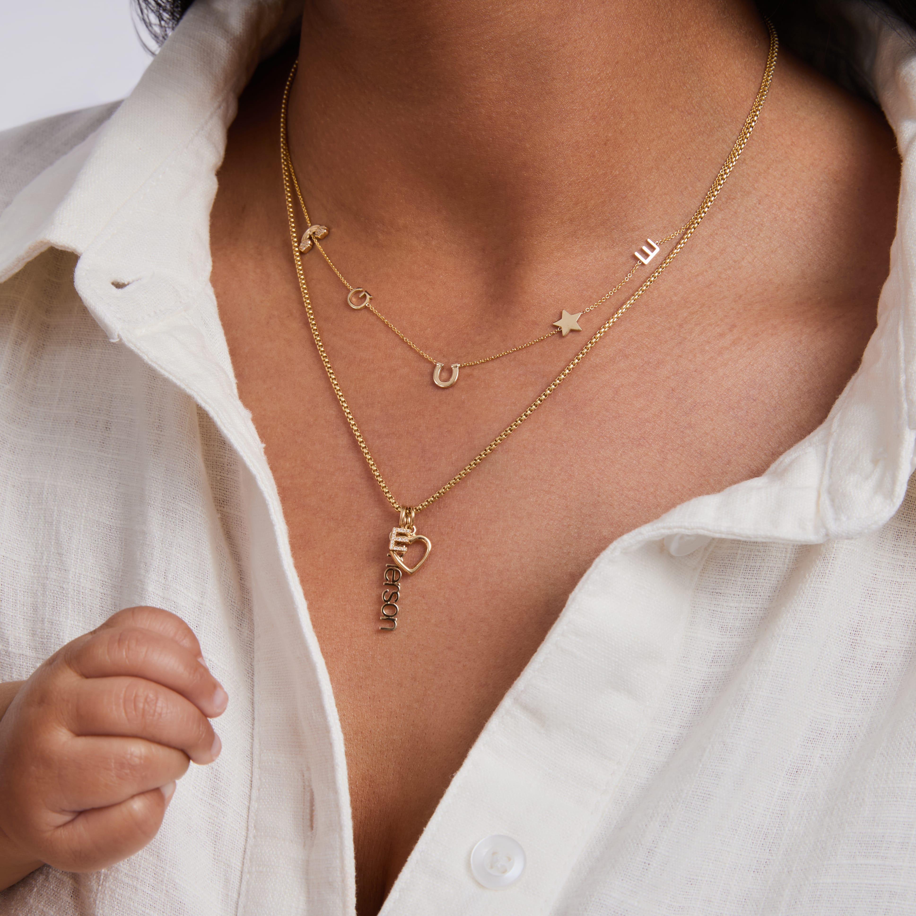 Close-up of a person wearing a gold necklace with various charms against a white shirt background.
