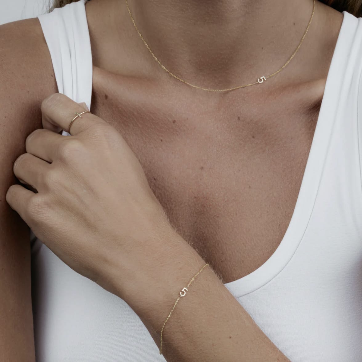 Close-up of a person wearing gold necklaces and a ring on a plain 