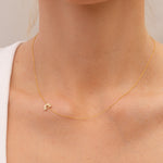 Gold necklace with a small pavé diamond rainbow charm on a person's neck against a neutral background