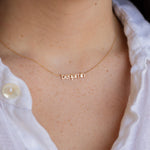 A close-up of a person wearing a delicate gold chain necklace with the name 'benjamin' spelled out in lowercase cursive letters, styled with a white button-down shirt.