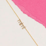 Gold 'mimi' necklace on a white and pink background