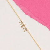 Gold 'mimi' necklace on a white and pink background