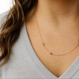 Gold necklace with a letter 'B' pendant on a person wearing a light gray sweater.