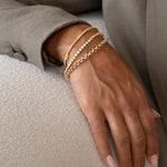 A close up of a woman wearing two gold diamond tennis bracelets and two gold chain link bracelets 