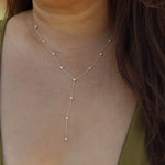 A delicate gold Y-necklace with small white pearl-like beads, shown worn on a model's neck and upper chest.