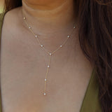 A delicate gold Y-necklace with small white pearl-like beads, shown worn on a model's neck and upper chest.