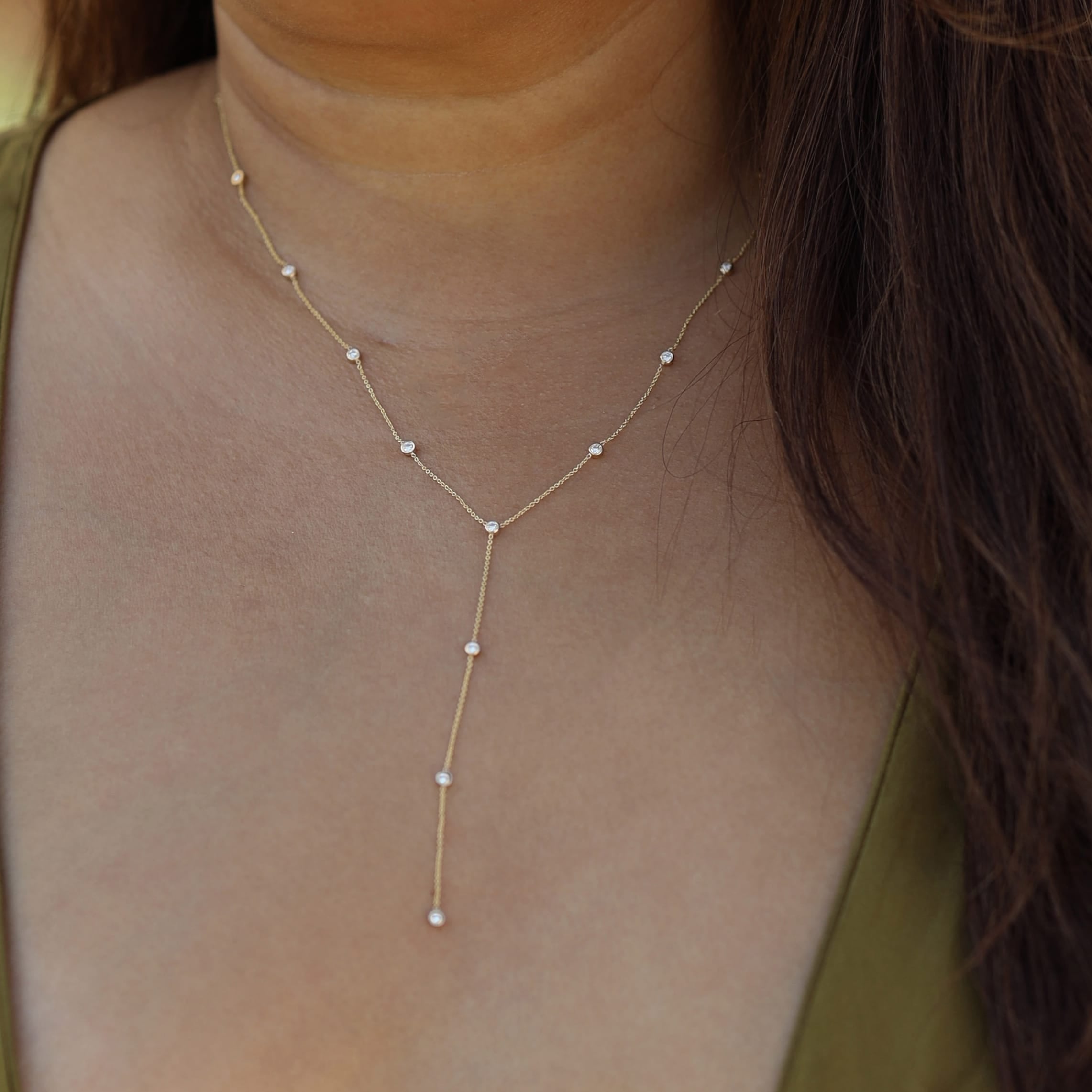 A delicate gold Y-necklace with small white pearl-like beads, shown worn on a model's neck and upper chest.