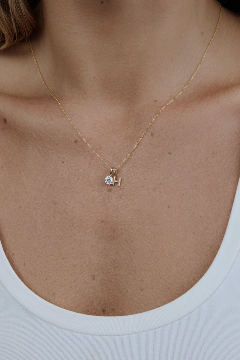 Gold necklace with a small pendant on a person wearing a white tank top.