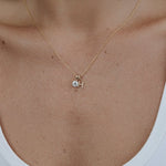 Gold necklace with a small pendant on a person wearing a white tank top.