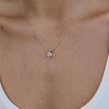 Gold necklace with a small pendant on a person wearing a white tank top.