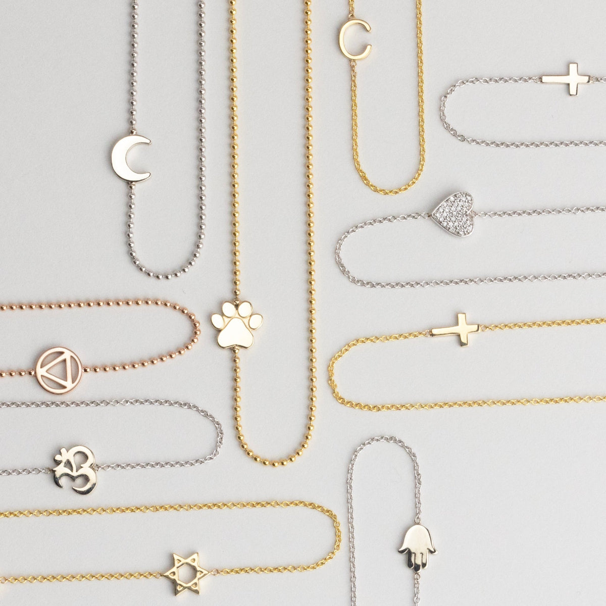 Collection of yellow and white gold  necklaces with various charms on a light grey background