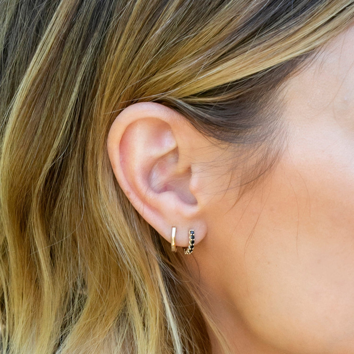 Close-up of an ear wearing a gold hoop earring with black accents.
