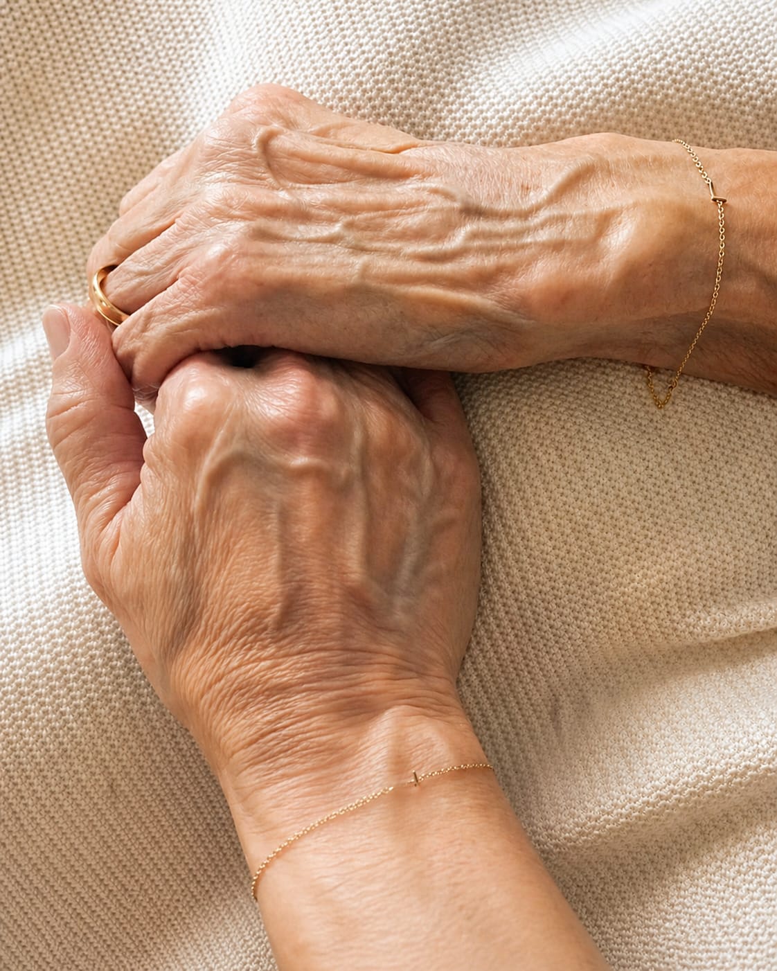 Close-up of two elderly hands holding each other on a textured beige background