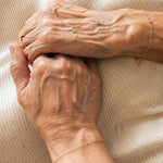 Close-up of two elderly hands holding each other on a textured beige background