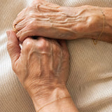 Close-up of two elderly hands holding each other on a textured beige background