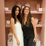two women posing in front of a shelf wearing crystal pendents