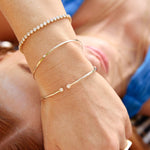 Close-up of a person's wrist wearing three gold bracelets with diamonds