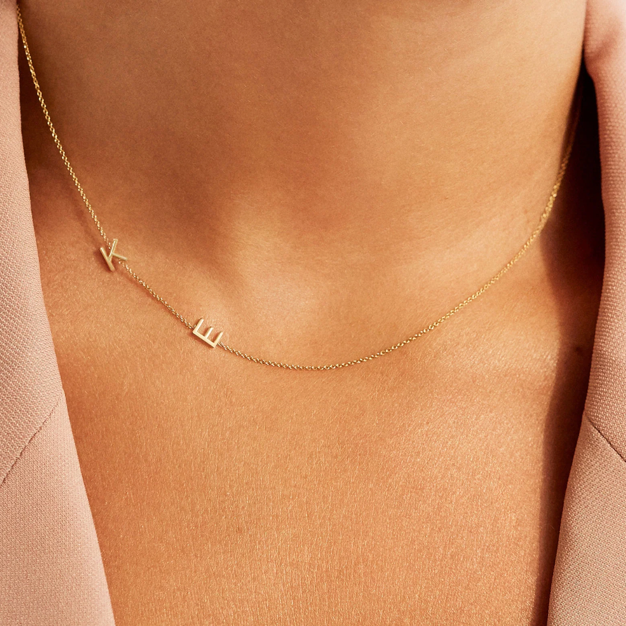 Gold necklace with letter 'K'  and 'E' charm on a person wearing a pink top.