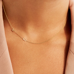 Gold necklace with letter 'K'  and 'E' charm on a person wearing a pink top.