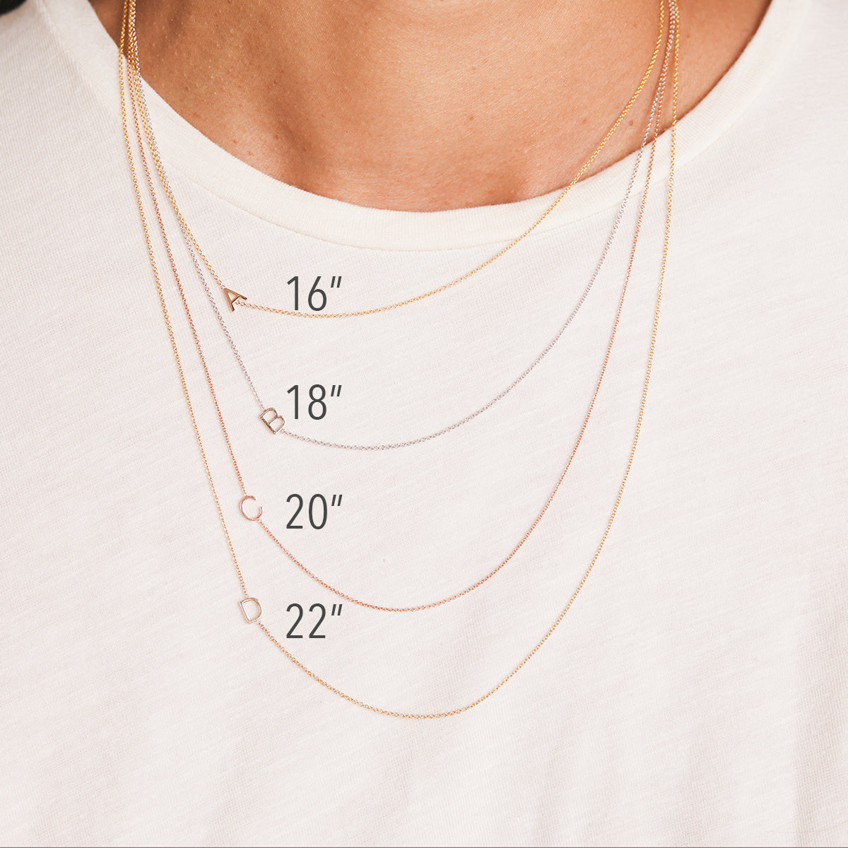 Gold necklaces of different lengths displayed on a white shirt.