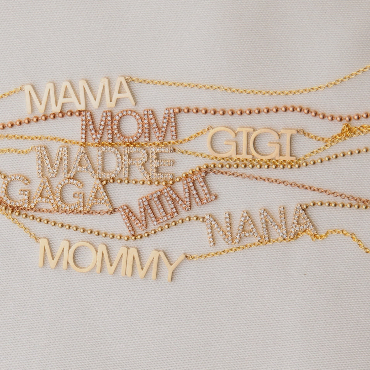 Gold necklaces with various mother wordplate necklaces on a light gray background