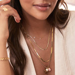 Close-up of a woman wearing multiple gold necklaces with a blurred background