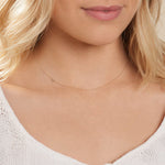A close-up of a woman's neck wearing a white gold necklace with a letter X charm.