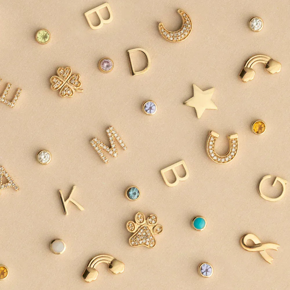 assortment of Yellow Gold letters, charms and birthstone on beige background