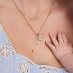 Close-up of a necklace with a heart-shaped pendant and 'Mason' engraved, worn by a person with a baby's hand touching the chest.