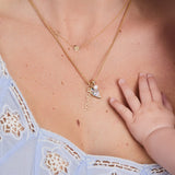 Close-up of a necklace with a heart-shaped pendant and 'Mason' engraved, worn by a person with a baby's hand touching the chest.