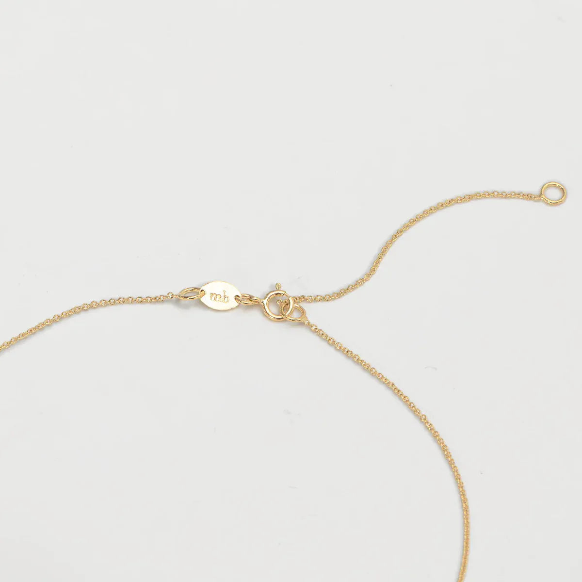 The back of a necklace in yellow gold on an off-white background. 