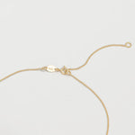 The back of a necklace in yellow gold on an off-white background. 
