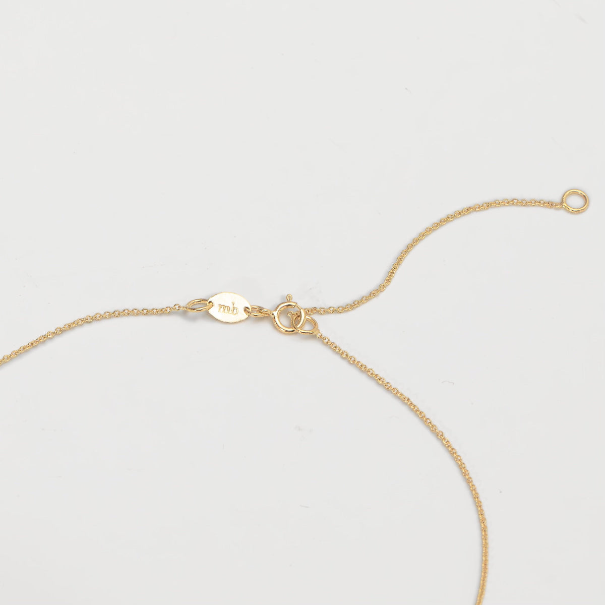Gold necklace showing the adjustable jump ring on a light gray background