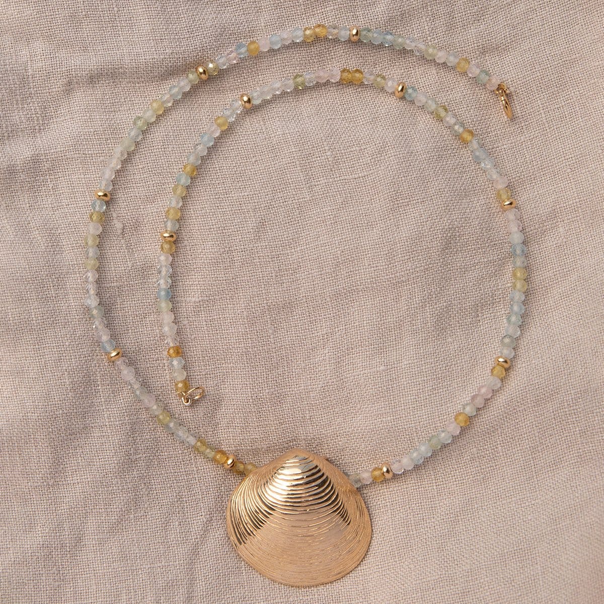 An Endless Summer Necklace - Saint-Tropez with The Golden Venus Shell on a beige fabric background. 
