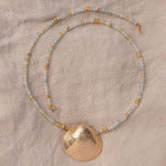 An Endless Summer Necklace - Saint-Tropez with The Golden Venus Shell on a beige fabric background. 