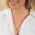 Close-up of a blonde woman wearing a Zodiac Necklace - Aquarius with a white shirt against a neutral background. 