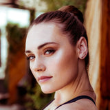 A woman wearing a Straight as an Arrow Earring with her hair in a bun and gold necklaces, against a blurred background. 
