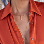 A woman's decellotage wearing an Omega Chain with a Balance Crystal Charm in Rose Quartz and a Zodiac Necklace - Cancer, styled in an orange shirt against a blurred background. 