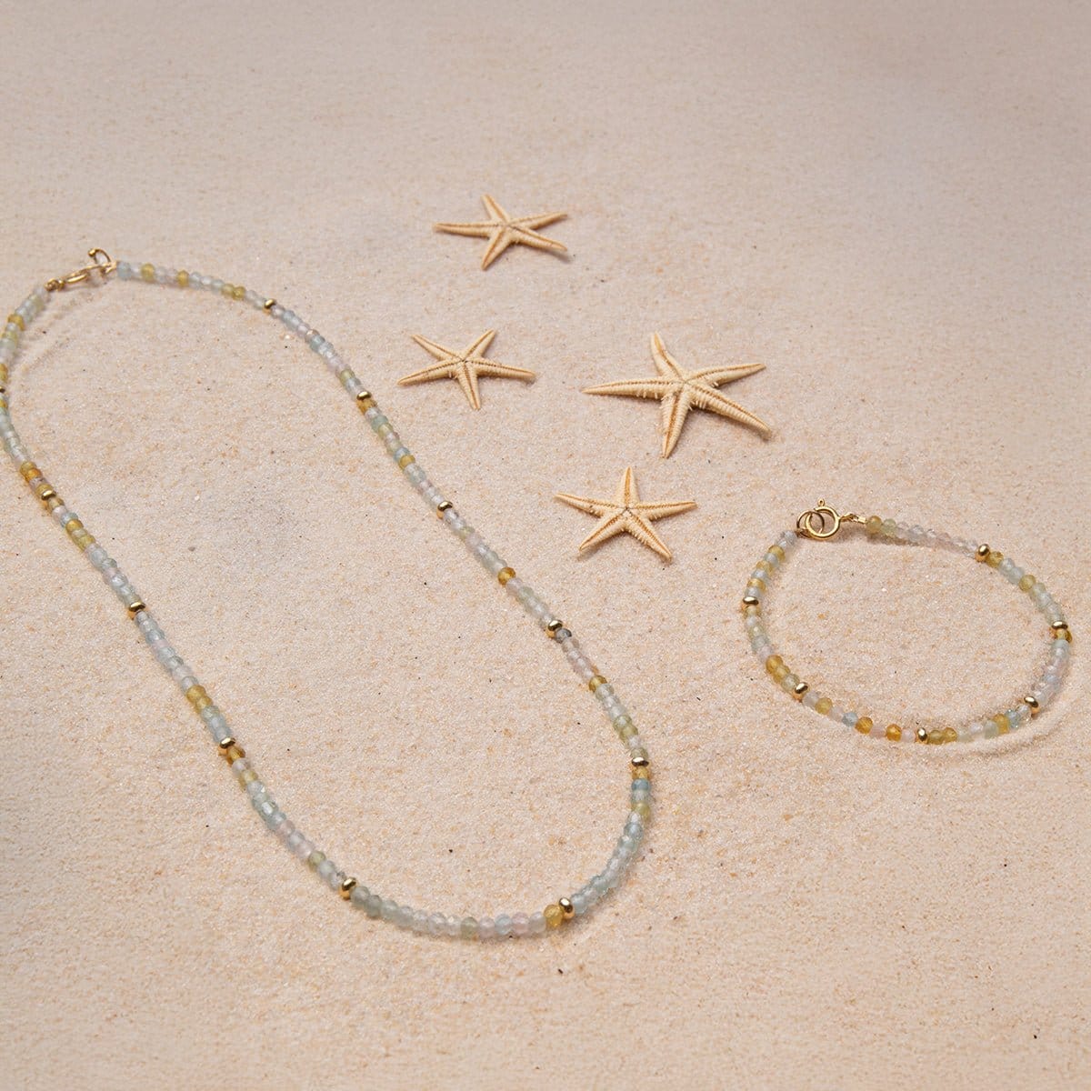 An Endless Summer Bracelet and Necklace in Saint-Tropez laid on sand with four starfishes.