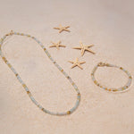 An Endless Summer Bracelet and Necklace in Saint-Tropez laid on sand with four starfishes.