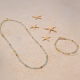 An Endless Summer Bracelet and Necklace in Saint-Tropez laid on sand with four starfishes.