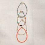 Four Endless Summer Bracelets (Blue Lagoon, Capri, Mykonos and Saint-Tropez) laid vertically on an off-white fabric background. 