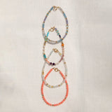 Four Endless Summer Bracelets (Blue Lagoon, Capri, Mykonos and Saint-Tropez) laid vertically on an off-white fabric background. 