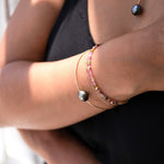 Close-up of a person’s arm wearing an Endless Summer Bracelet – Coral Reef, an Element Short Link Bracelet and a Baroque Black Pearl Bangle and Necklace, styled in a black top.