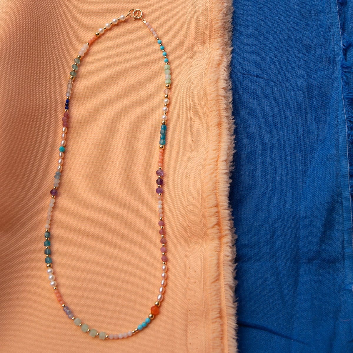 An Endless Summer Necklace - Capri against a blue and orange fabric background. 